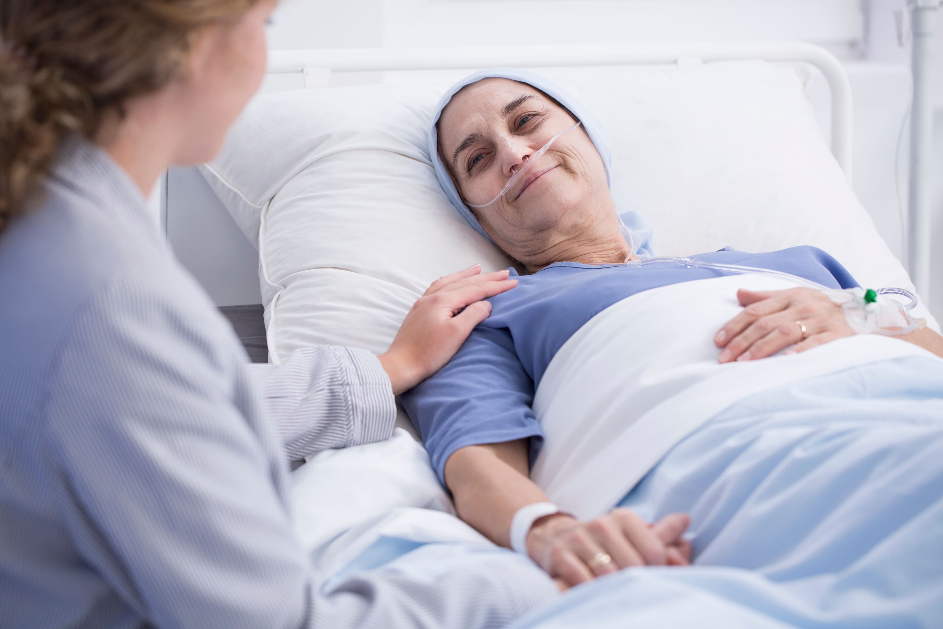 Leczenie paliatywne – pacjentka z nowotworem leży w łóżku, obok niej siedzi pielęgniarka